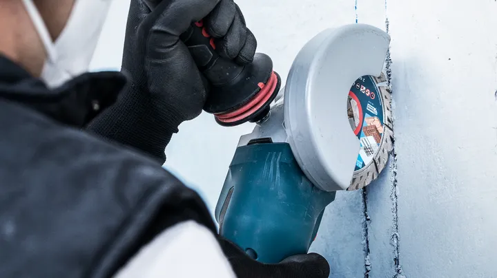 Object #200360654: 2793282_app_web_02 Một người mặc thiết bị an toàn sử dụng máy cắt điện để tạo rãnh trên tường.