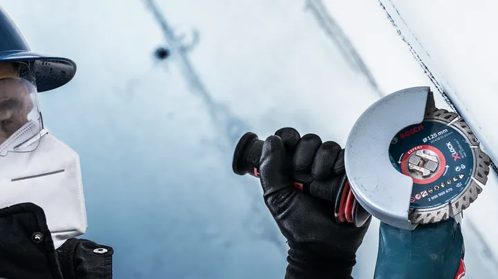 Object #200360655: 2793282_app_web_03 Một người mặc đồ bảo hộ sử dụng máy mài góc để cắt bề mặt kim loại.