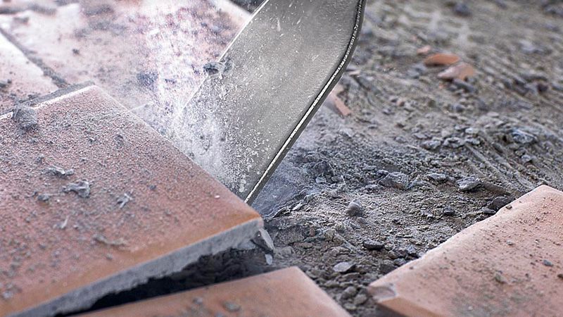 Máy đục gạch phá vỡ gạch men trên sàn nhà đầy bụi.