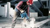 Một người mặc đồ bảo hộ đang vận hành búa phá dỡ để phá vỡ bê tông.