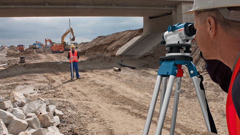 Người đeo thiết bị an toàn sử dụng máy thủy bình quang học tại công trường xây dựng đường bộ.