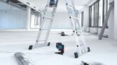 Thiết bị cân bằng laser chiếu những đường màu đỏ xuống sàn nhà bên dưới một người đang đứng trên thang.
