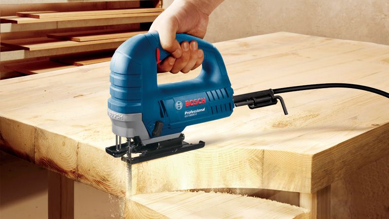 GST 8000 E Một người sử dụng máy cưa lọng để cắt một hình cong thành một tấm ván gỗ.