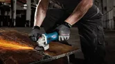 Một người mặc đồ bảo hộ đang mài kim loại, tạo ra tia lửa trên bàn làm việc.