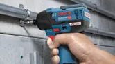 Một người đang cố định một ống kim loại vào tường bằng máy vặn vít không dây.