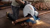 Một người mặc đồ bảo hộ đang cắt một ống kim loại bằng cưa kim loại, tia lửa bắn ra.