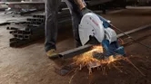 Một người mặc đồ bảo hộ dùng máy cưa cắt các thanh kim loại, tạo ra tia lửa.