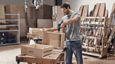 Một người mặc đồ bảo hộ đang lắp ráp ngăn kéo bằng gỗ bằng máy khoan không dây.