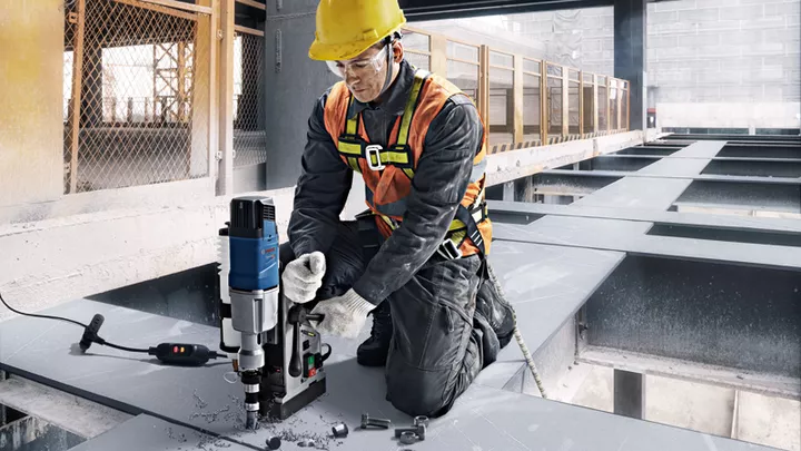 GBM 50-2 Một người mặc đồ bảo hộ đang khoan vào dầm thép tại một công trường xây dựng.