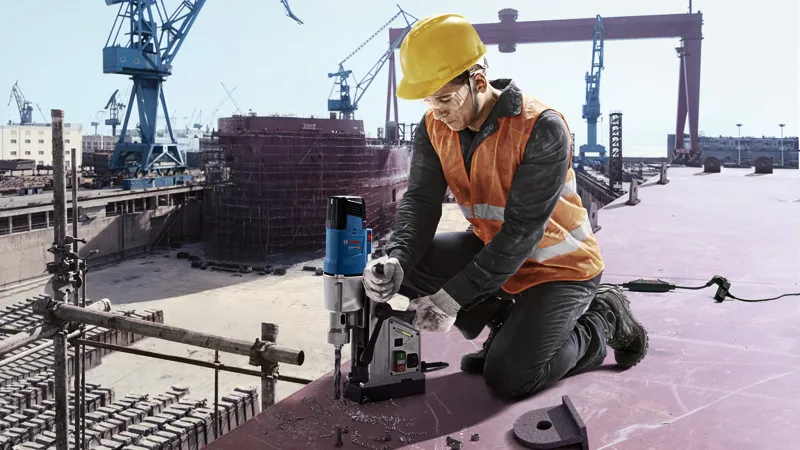 Một người mặc đồ bảo hộ đang vận hành máy khoan lõi từ tại một công trường xây dựng.