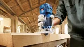Một người mặc đồ bảo hộ sử dụng máy phay cầm tay để tạo hình cạnh của một tấm ván gỗ.