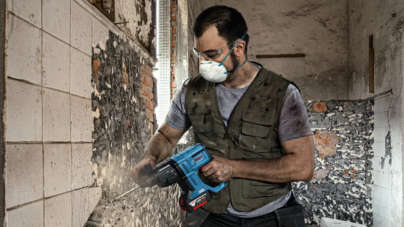 Một người mặc đồ bảo hộ đang dùng dụng cụ điện để tháo gạch ốp tường.