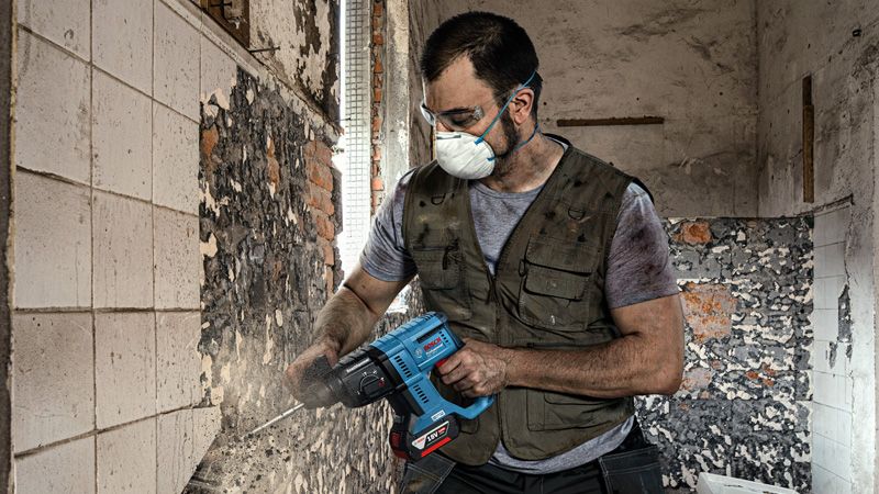 Một người mặc đồ bảo hộ đang dùng dụng cụ điện để tháo gạch ốp tường.