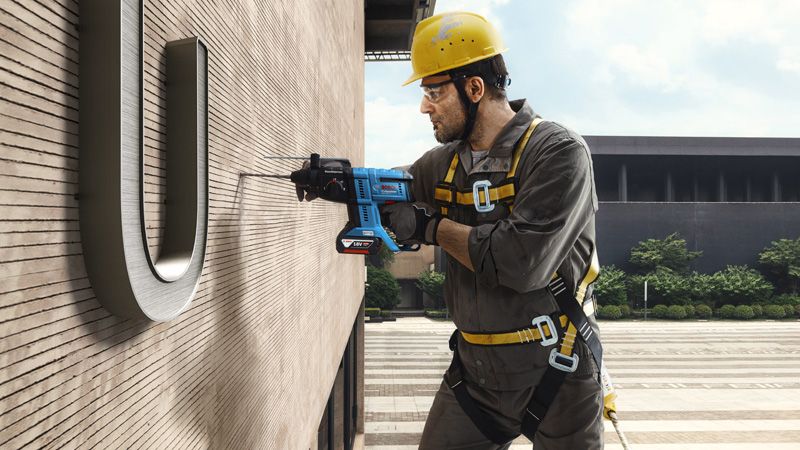 Một người mặc thiết bị an toàn khoan vào tường tòa nhà trong khi đang lơ lửng.