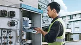 Một người mặc đồ bảo hộ đang sử dụng tua vít không dây trên bảng điện.