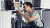 Một người đang sửa máy giặt bằng máy vặn vít không dây.