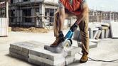 Một người mặc đồ bảo hộ đang sử dụng máy cắt điện để cắt khối bê tông tại công trường xây dựng.