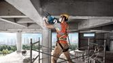 Một người mặc đồ bảo hộ đang phá dỡ một cột bê tông bằng búa phá dỡ.
