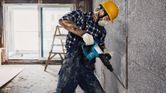 Một người mặc đồ bảo hộ đang sử dụng búa phá dỡ để phá vỡ bức tường bê tông.
