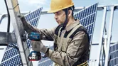 Một người mặc đồ bảo hộ đang sử dụng cờ lê lực không dây để siết chặt khung tấm pin mặt trời bằng kim loại.