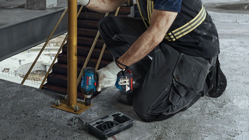 GDS 18V-400 Một người mặc đồ bảo hộ đang siết chặt bu lông trên một trụ kim loại bằng cờ lê lực không dây.