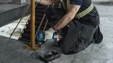 Một người mặc đồ bảo hộ đang siết chặt bu lông trên một trụ kim loại bằng cờ lê lực không dây.