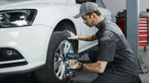 Một người mặc thiết bị an toàn sử dụng cờ lê lực không dây để siết chặt bu lông bánh xe trên ô tô.