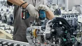 Một người mặc thiết bị an toàn đang sử dụng cờ lê tác động không dây để tháo cụm động cơ.