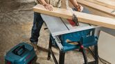 Một người mặc đồ bảo hộ đang cắt gỗ bằng máy cưa bàn trong xưởng.