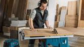 Một người mặc đồ bảo hộ đang cắt gỗ bằng máy cưa bàn trong xưởng.