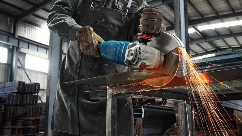 Một người mặc đồ bảo hộ đang cắt tấm kim loại bằng máy mài góc lớn, tia lửa bắn ra.