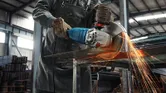 Một người mặc đồ bảo hộ đang cắt tấm kim loại bằng máy mài góc lớn, tia lửa bắn ra.