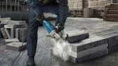 Một người mặc đồ bảo hộ đang cắt khối bê tông bằng máy cắt điện.