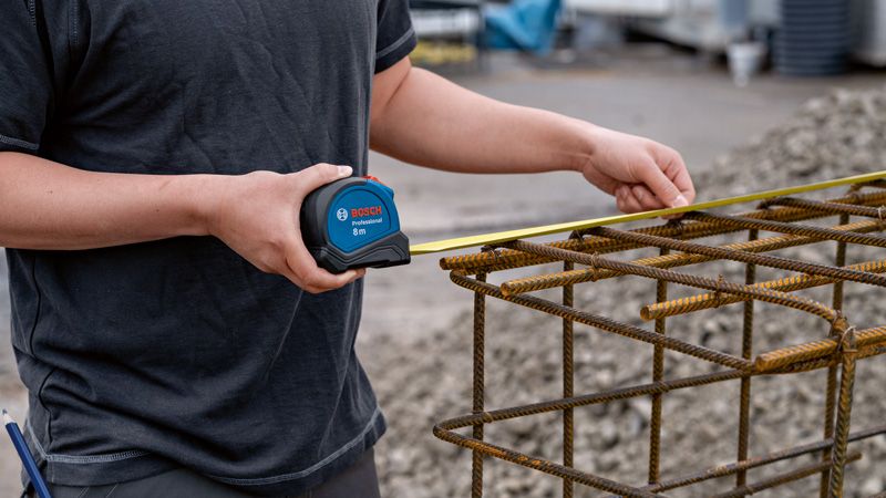 Một người sử dụng thước dây để kiểm tra chiều rộng của một kết cấu cốt thép bằng kim loại.