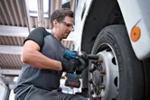 Một người mặc thiết bị an toàn sử dụng cờ lê lực không dây để siết chặt bu lông bánh xe tải.