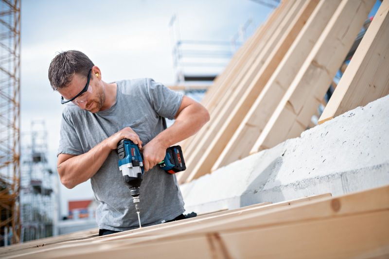 Người đeo thiết bị an toàn sử dụng cờ lê lực không dây để vặn vít vào gỗ.