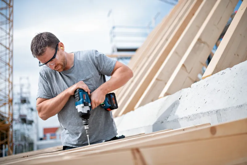 Người đeo thiết bị an toàn sử dụng cờ lê lực không dây để vặn vít vào gỗ.