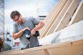 Người đeo thiết bị an toàn sử dụng cờ lê lực không dây để vặn vít vào gỗ.