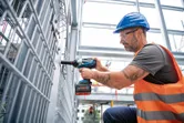 Một người mặc thiết bị an toàn sử dụng cờ lê lực không dây để siết chặt hàng rào kim loại.