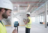 Hai người mặc thiết bị an toàn sử dụng máy đo laser và máy tính bảng bên trong tòa nhà đang xây dựng.