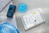 Đo bằng tia laser bên cạnh bản thiết kế và máy tính bảng hiển thị sơ đồ mặt bằng kỹ thuật số.