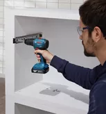 Người đeo thiết bị an toàn sử dụng máy khoan không dây để lắp thanh trượt ngăn kéo vào tủ.