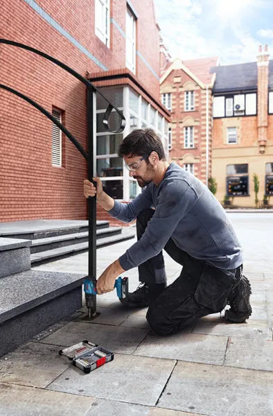 Một người mặc đồ bảo hộ đang khoan vào bậc đá, lắp lan can bằng kim loại.