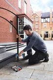 Một người mặc đồ bảo hộ đang khoan vào bậc đá, lắp lan can bằng kim loại.