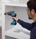 Một người mặc đồ bảo hộ sử dụng máy khoan không dây để lắp thanh ray tủ.