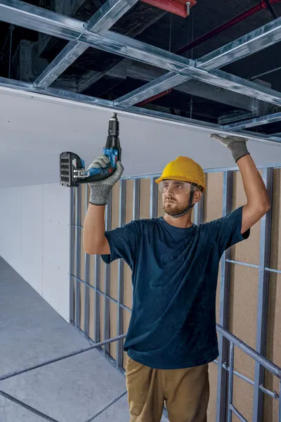 Người đeo thiết bị an toàn đang lắp đặt vách thạch cao bằng tua vít không dây.