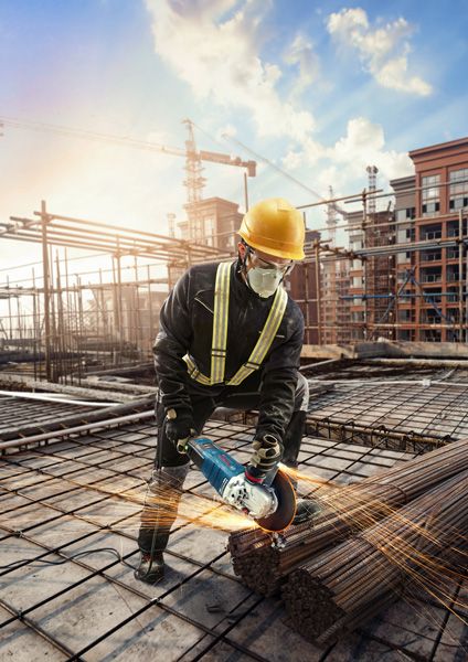 Một người mặc đồ bảo hộ đang sử dụng máy mài góc để cắt thanh thép tại công trường xây dựng.