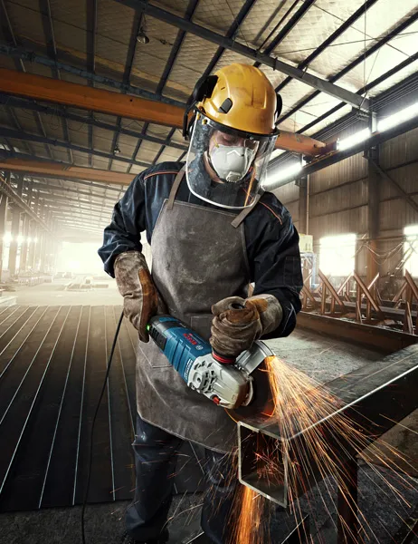 Một người mặc đồ bảo hộ đang mài kim loại, tạo ra tia lửa sáng trong nhà máy.