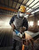 Một người mặc đồ bảo hộ đang mài kim loại, tạo ra tia lửa sáng trong nhà máy.