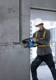 Một người mặc đồ bảo hộ đang khoan vào tường bê tông bằng máy khoan quay không dây.